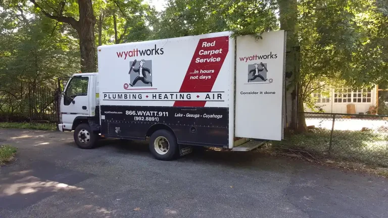 Homeowner and plumber discussing a water heater repair beside a residential tank in a utility closet.