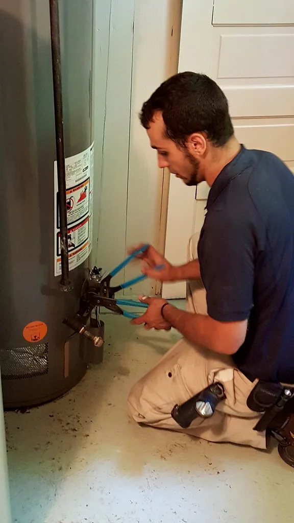 Hand holding a warranty document near a water heater drain valve and pipe connections.