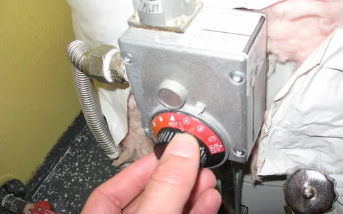 Multimeter probes checking a water heater thermostat terminal next to insulated wires